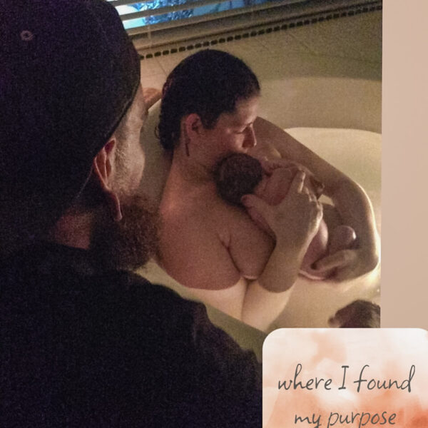 A father looking over the mother of his child holding a newborn in the home birth tub