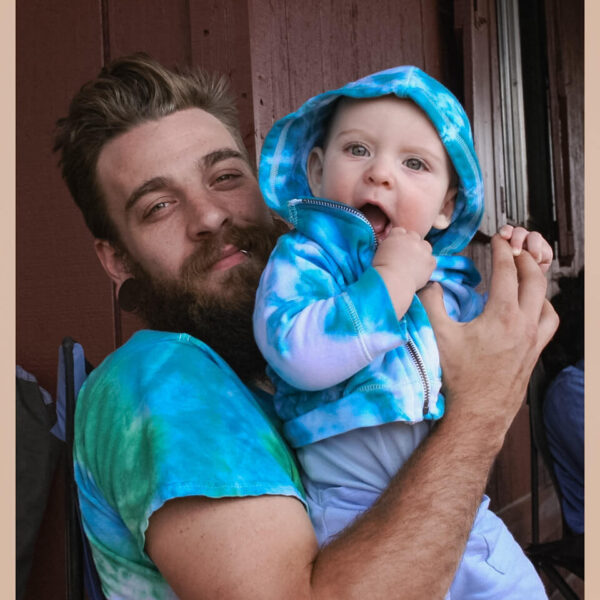 American father holding his infant son wearing tie-dye