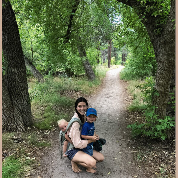young mother with toddler baby wearing infant barefoot on a hike in the woods